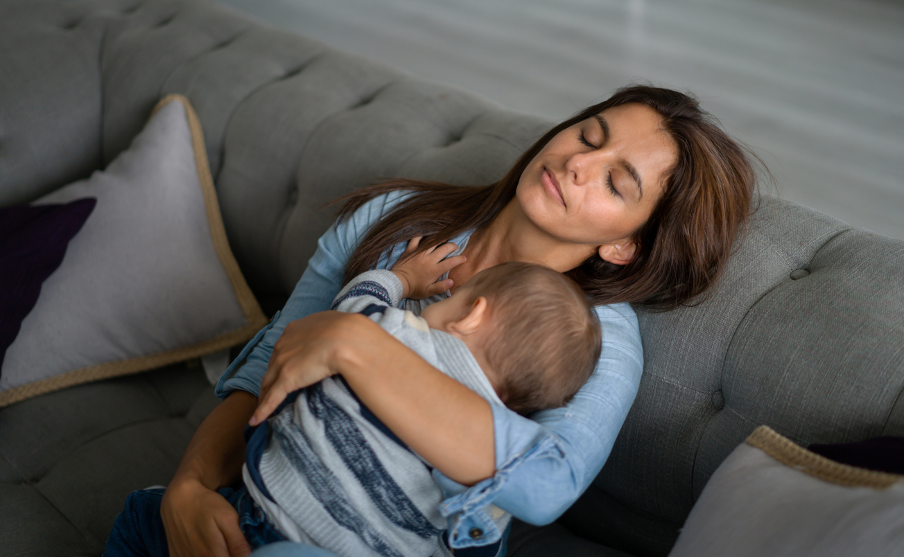 Exhausted mother sleeping in the sofa whole holding her baby - postpartum depression concepts 