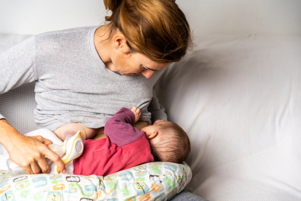 Mother breastfeeding her newborn baby while using a manual breast pump.